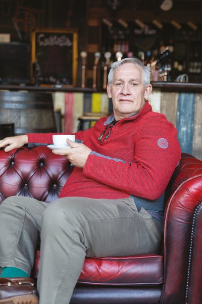 Man seated red Chesterfield sofa holding cup of tea