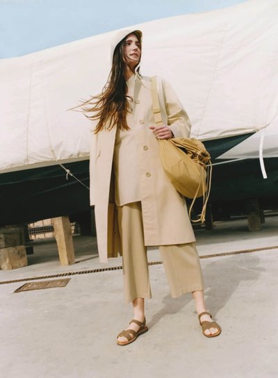 A woman wearing a Uniqlo U hooded coat, shirt and Gaucho trousers, holding a drawstring bag