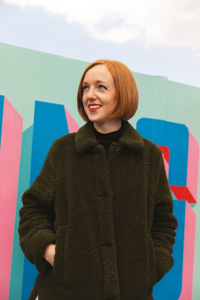 Woman in brown wool coat against a colourful mural background